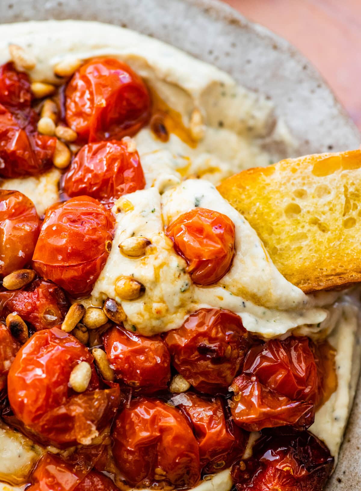 hand holding crostini with white bean dip and tomatoes on it.