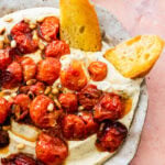 hand holding crostini with white bean dip and tomatoes on it.