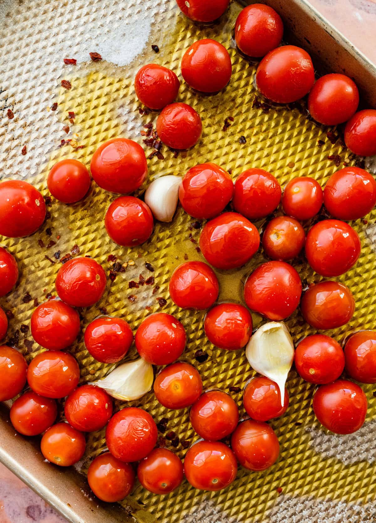 uncooked tomatoes and garlic on a cookie sheet with olive oil.