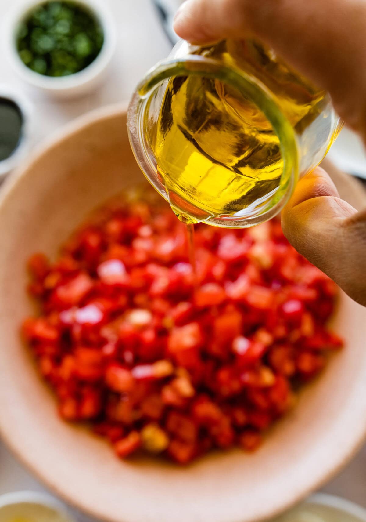 A person pouring olive oil over a bowl of chopped tomatoes.