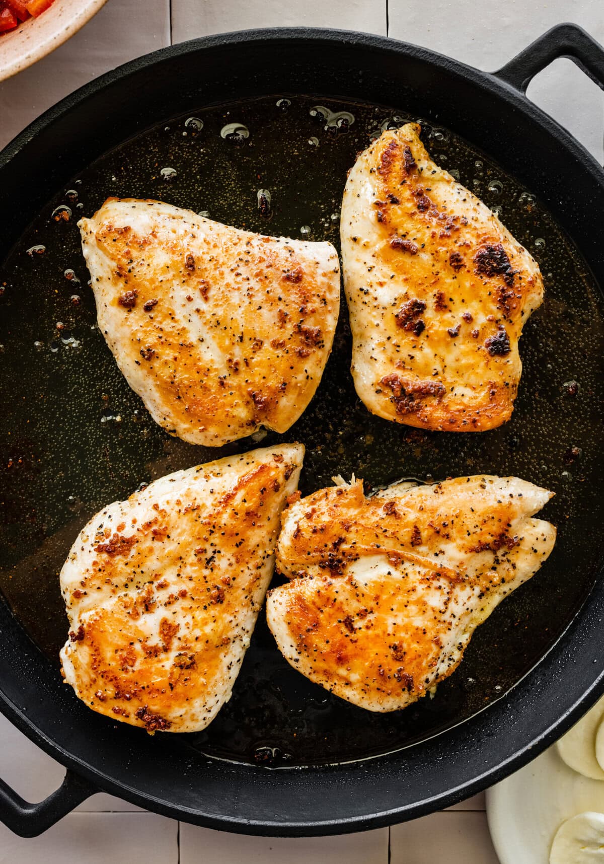 Four chicken breasts in a skillet on a table.