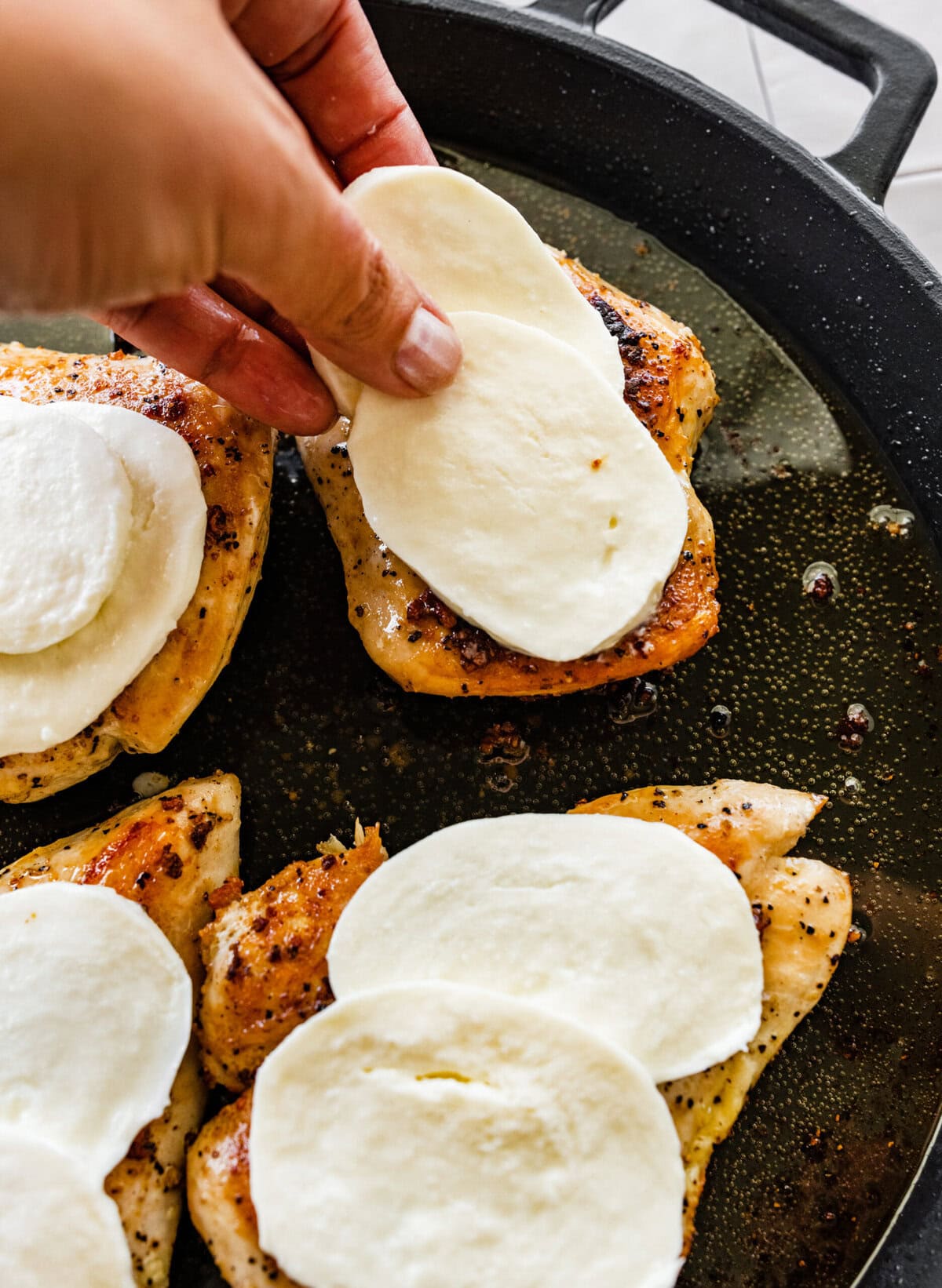 A person is putting mozzarella cheese on chicken.