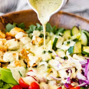 Hand holding a bowl of salad dressing pouring over salad.