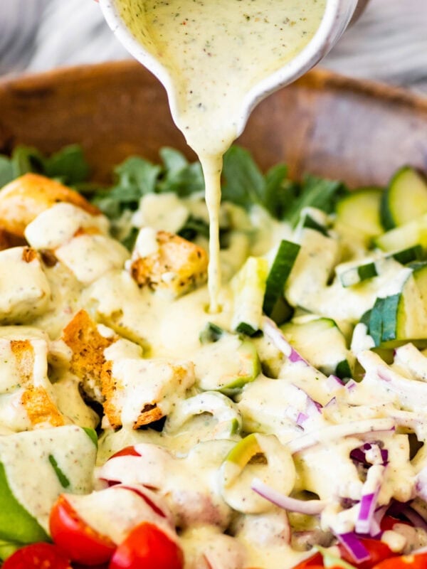 Hand holding a bowl of salad dressing pouring over salad.