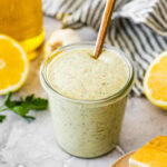 Garlic herb dressing in a jar with a spoon in it.