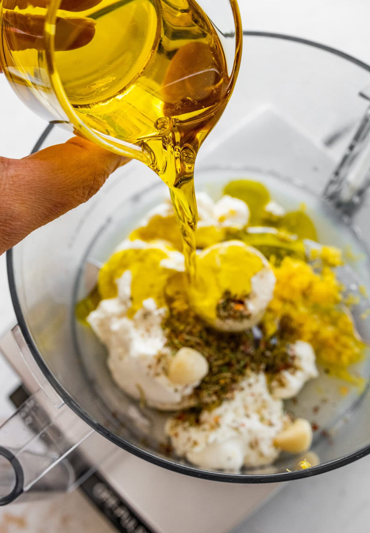 A hand pouring olive oil into a bowl of food