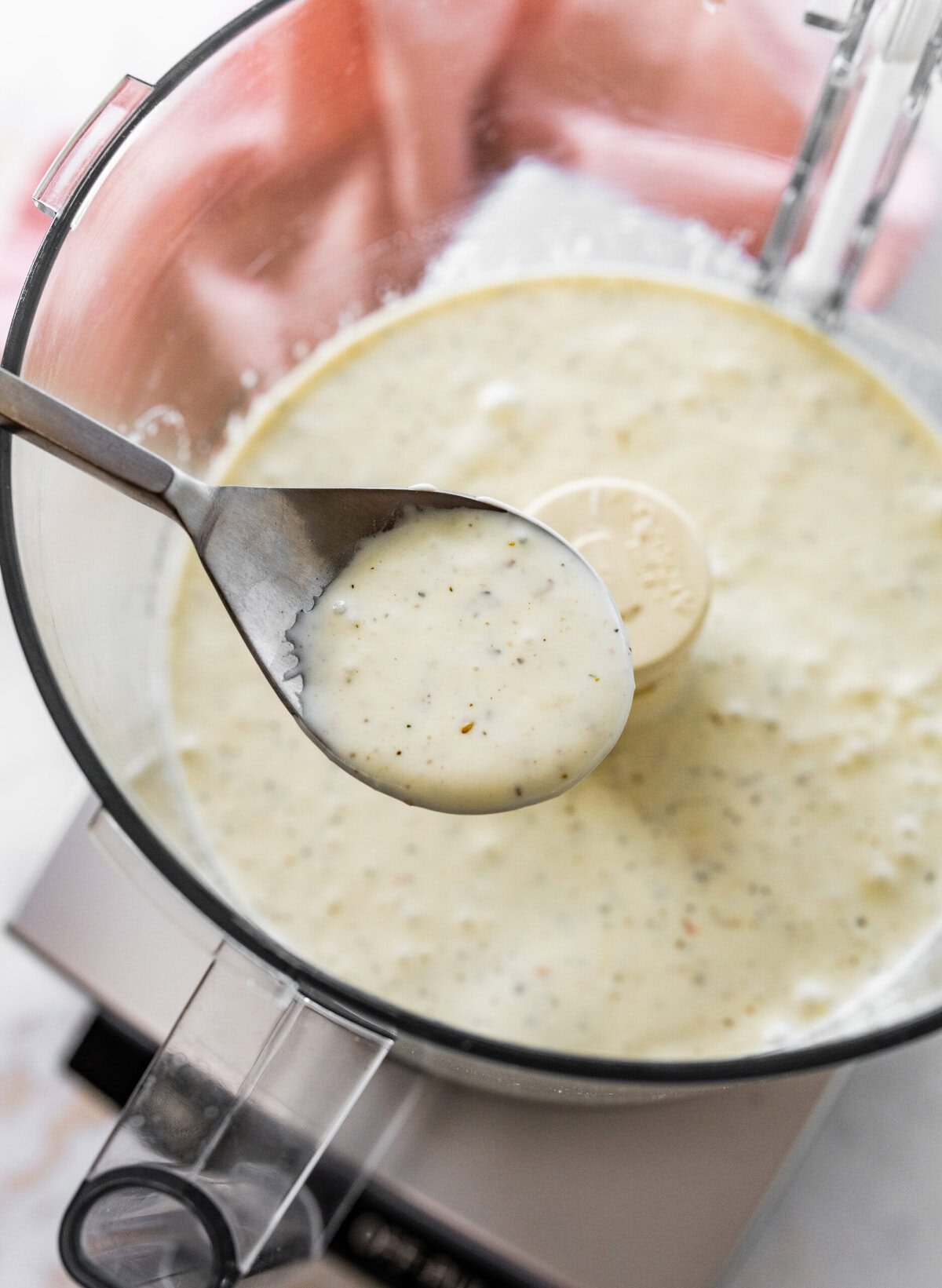 A spoon is in a food processor with a bowl of ricotta dressing.