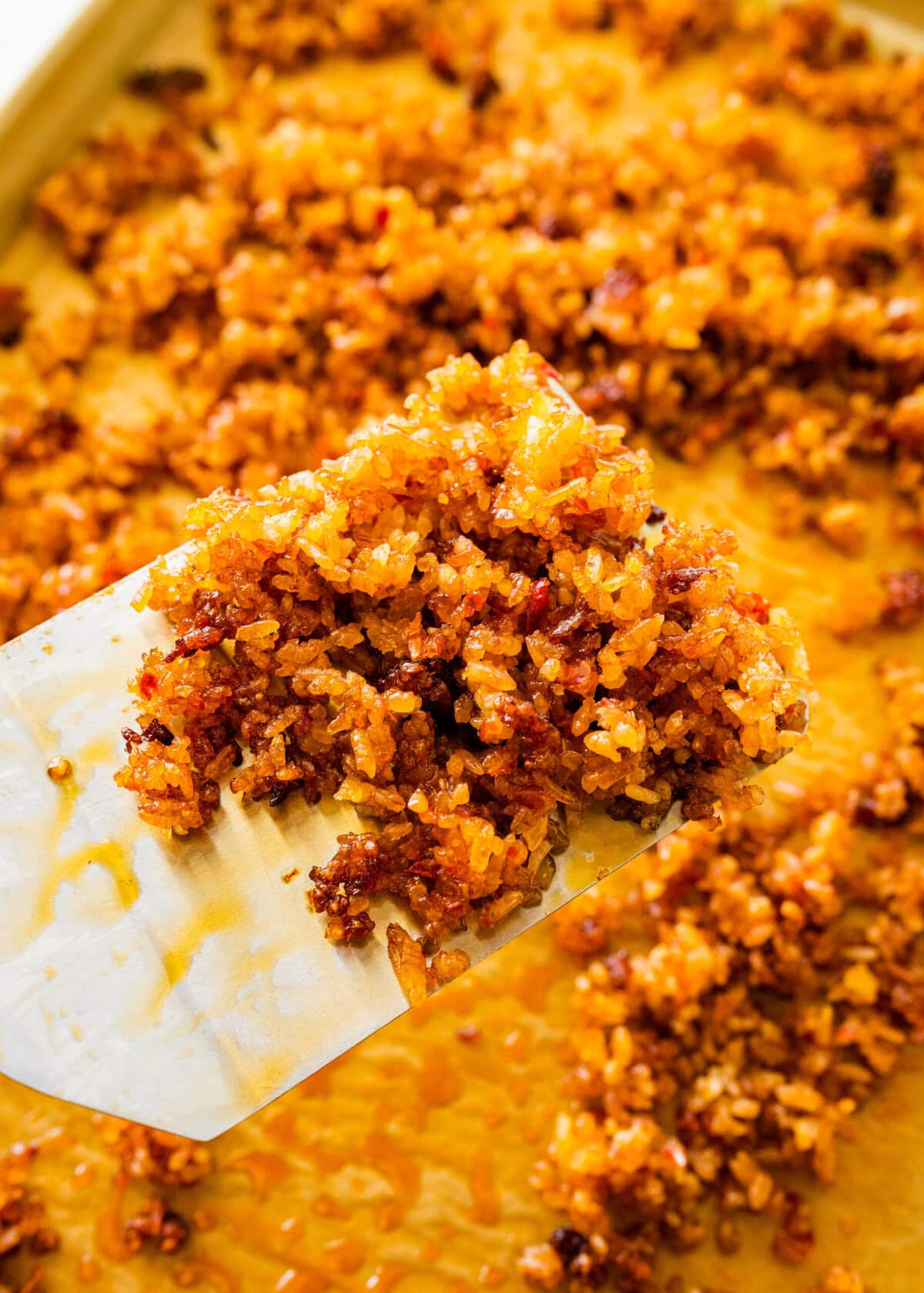 A spatula is lifting up crispy rice from pan.