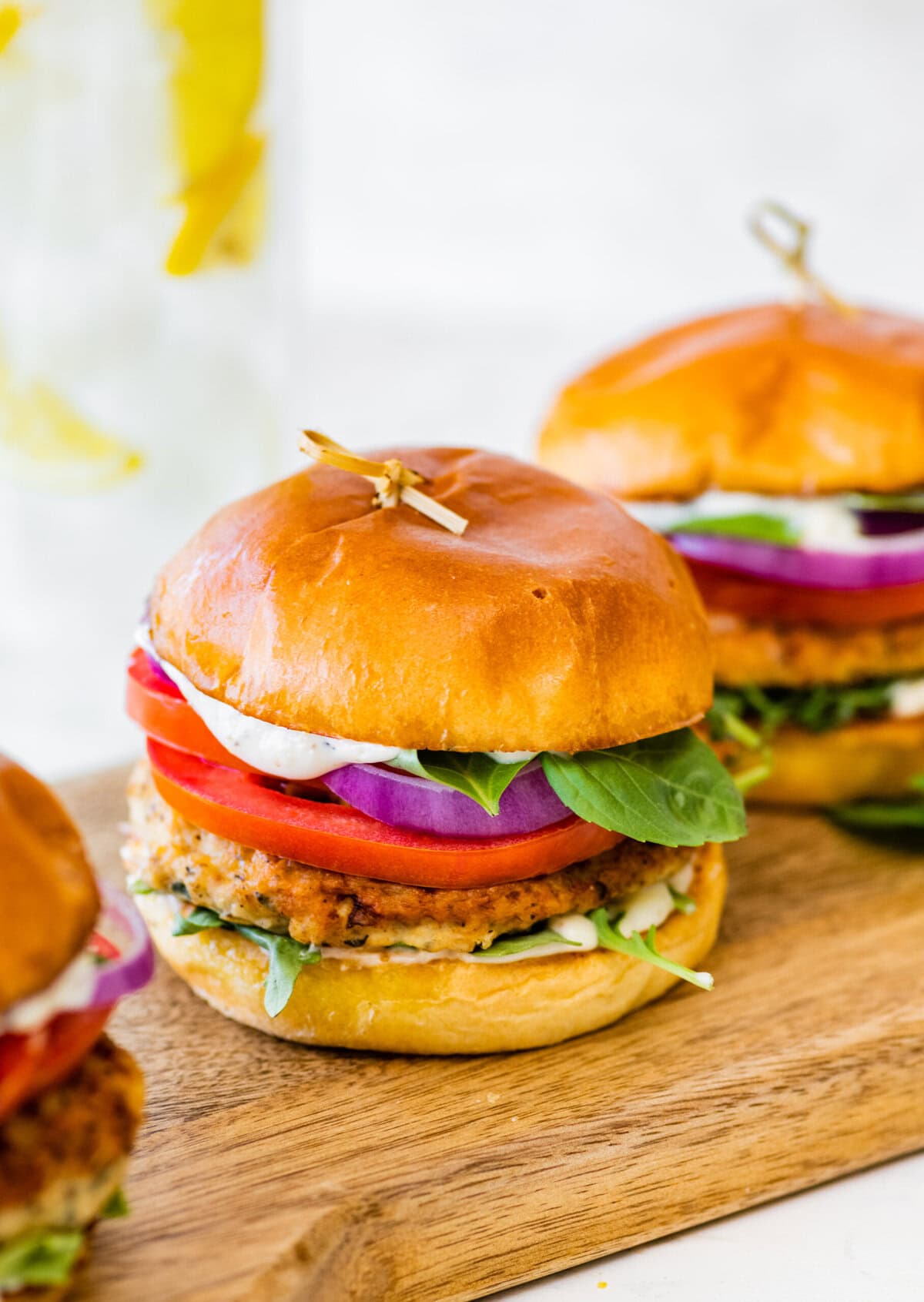 A wooden cutting board with three chicken burgers on it.