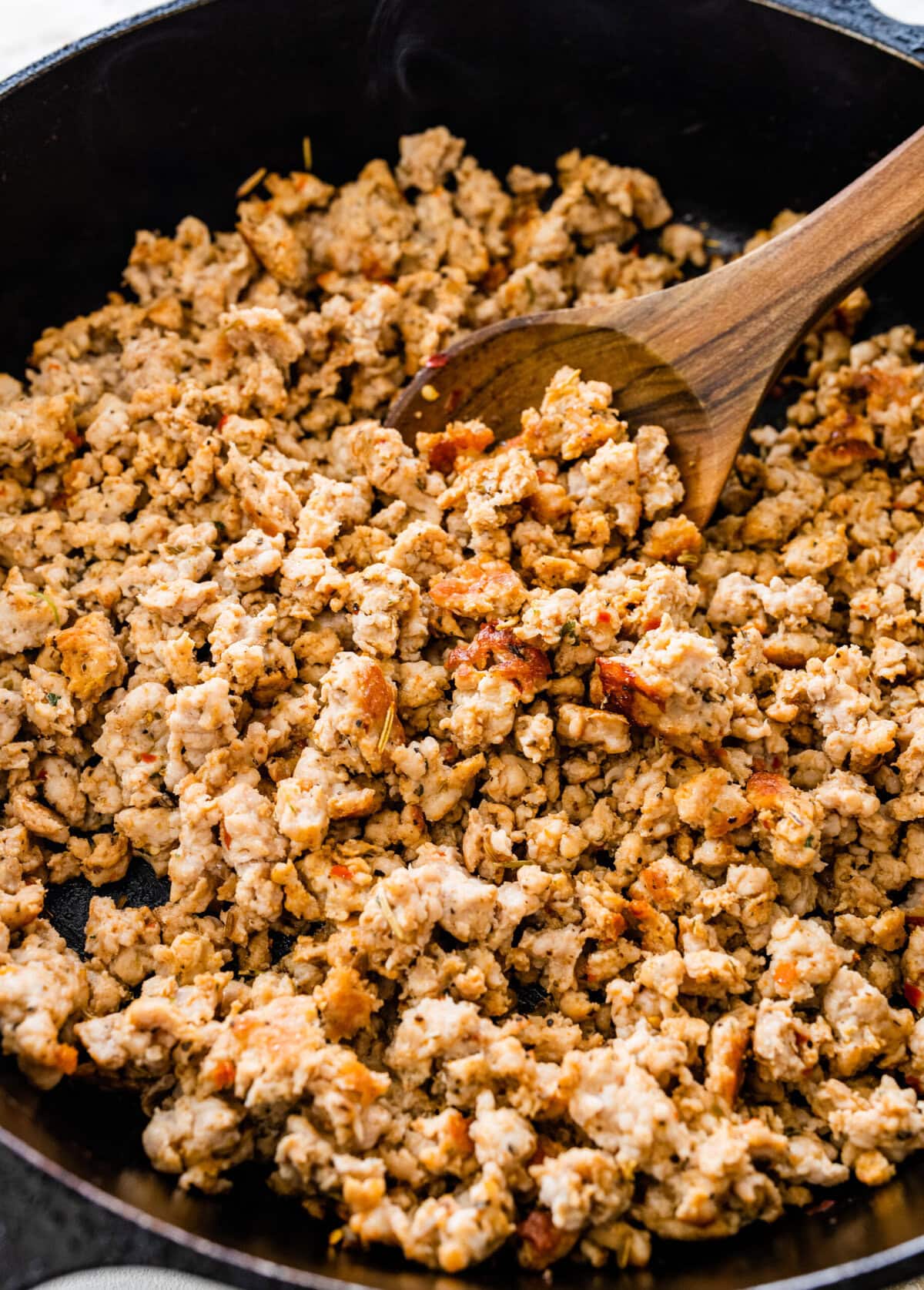 cooked homemade Italian sausage in a pan with wooden utensil in it.