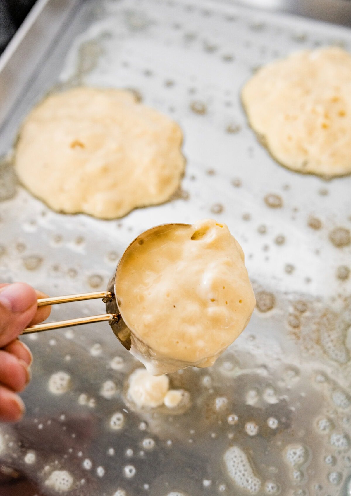 A person holding a spoon over a pan of pancakes