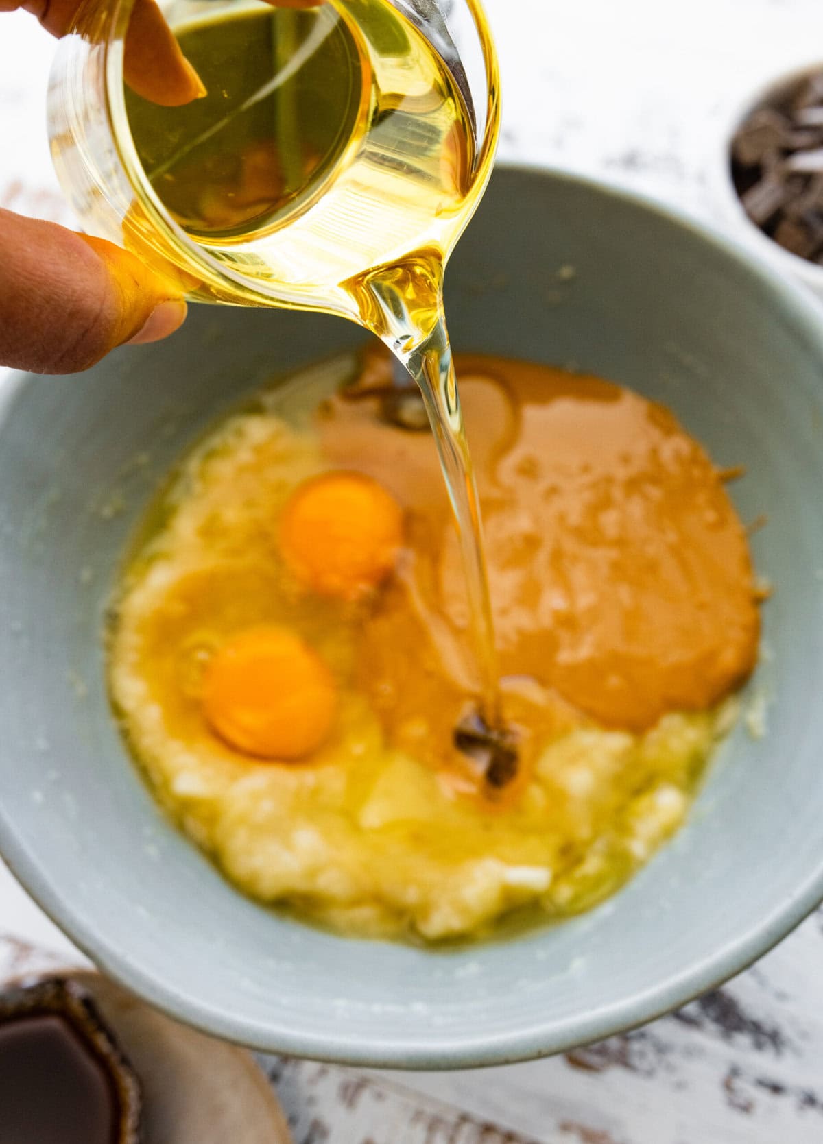 A person pouring oil into a bowl mashed bananas and peanut butter.
