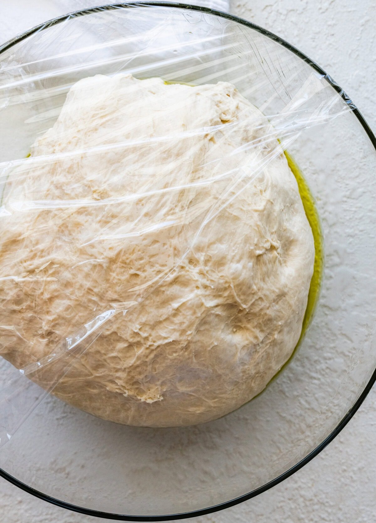 A round ball of dough in a glass bowl ready to rest in the fridge.