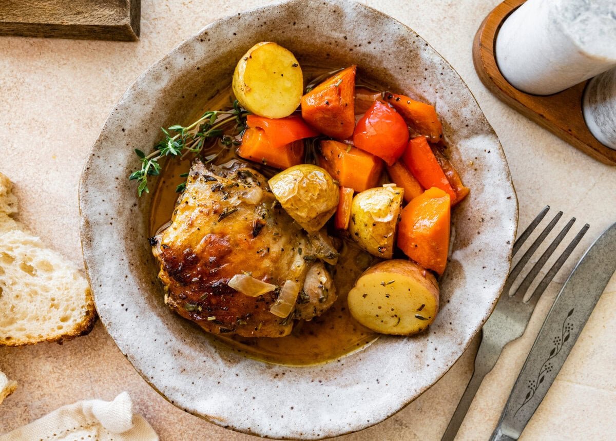 Chicken with potatoes and carrots in a white bowl.