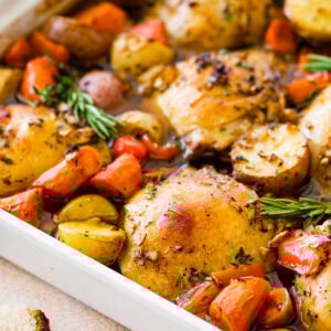 A pan of baked chicken, potatoes, carrots and other vegetables.