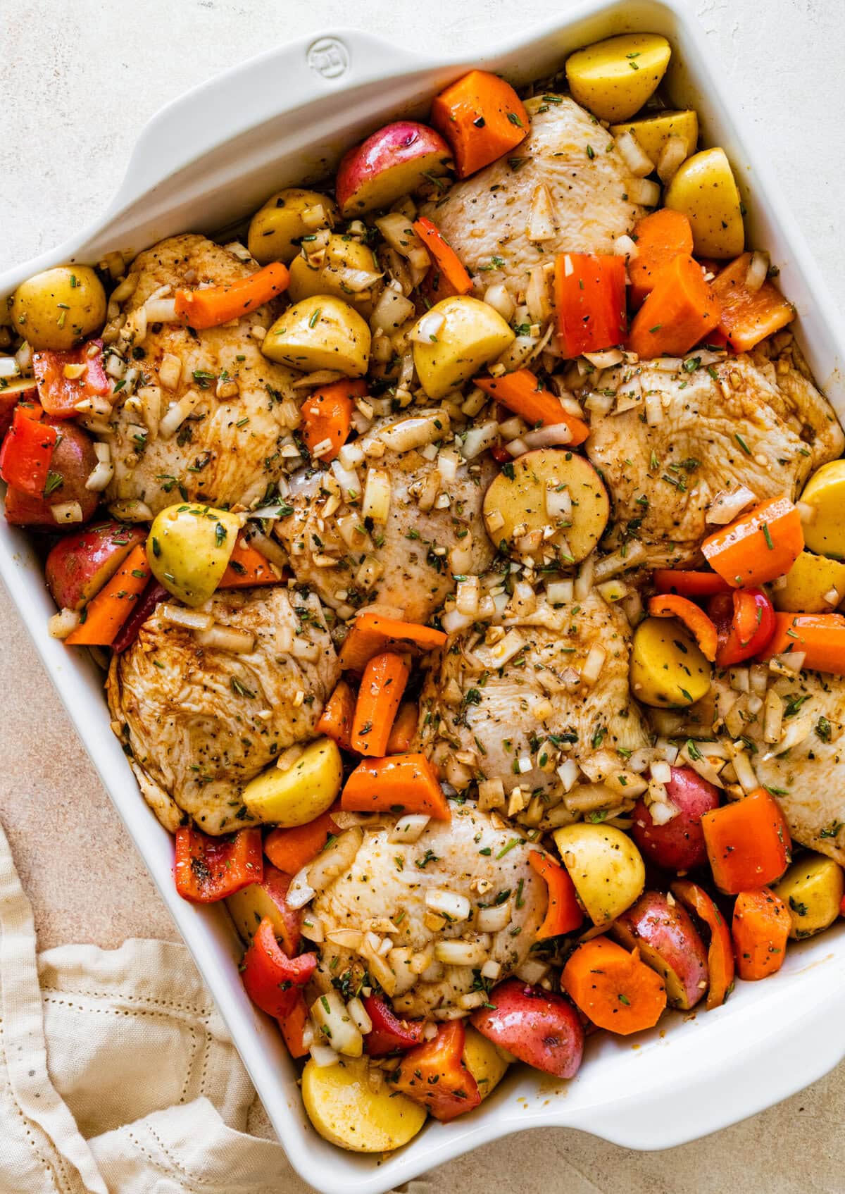 A white casserole dish filled with chicken, potatoes and vegetables.