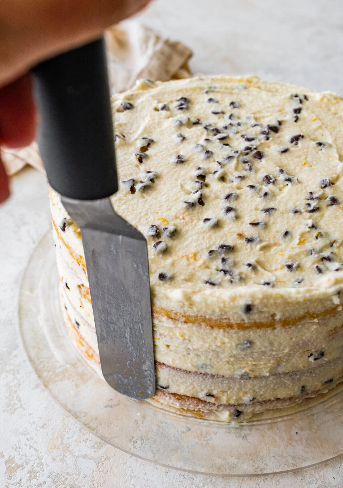 Frosting the cannoli cake with a cake spatula.