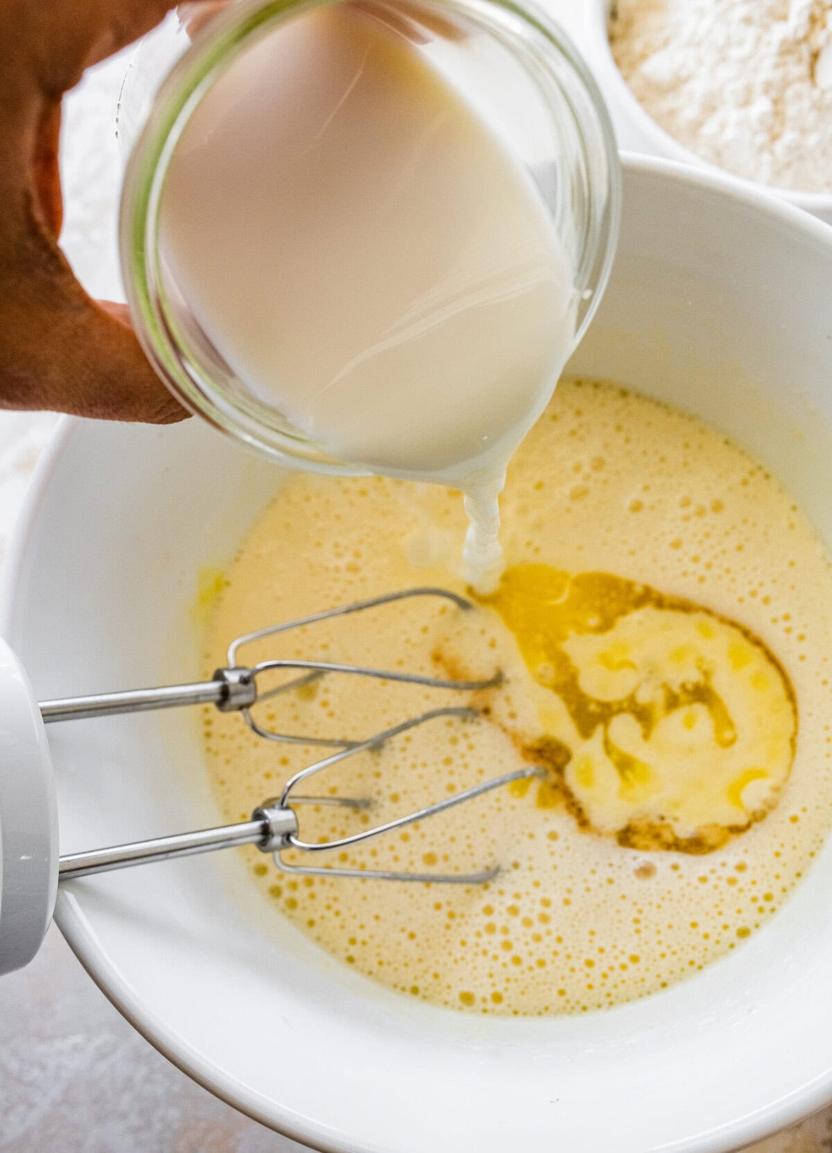 A person pouring milk into a bowl with eggs and flour.