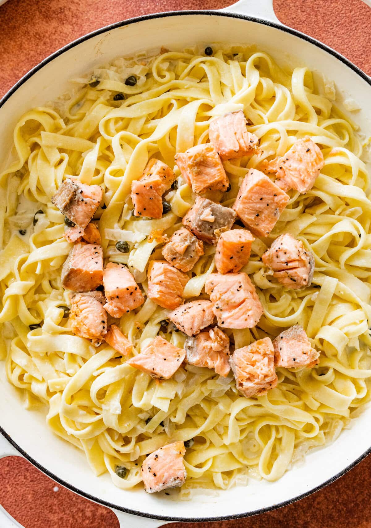 Adding the cooked salmon cubes in the pan with the pasta and sauce.