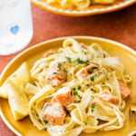 Salmon and lemon pasta on an orange plate.