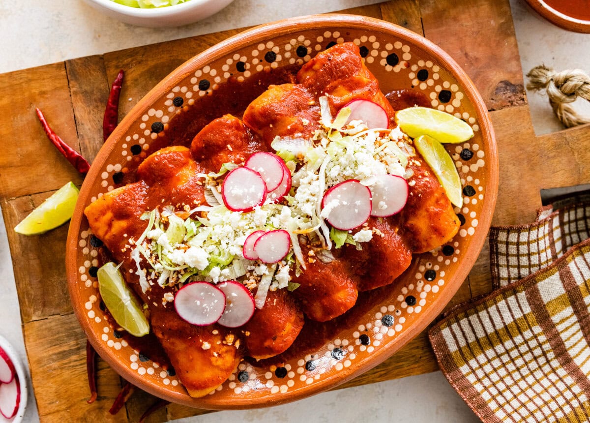 rolled enchiladas rojas or red enchiladas on a Mexican platter with radishes and cheese on top. 