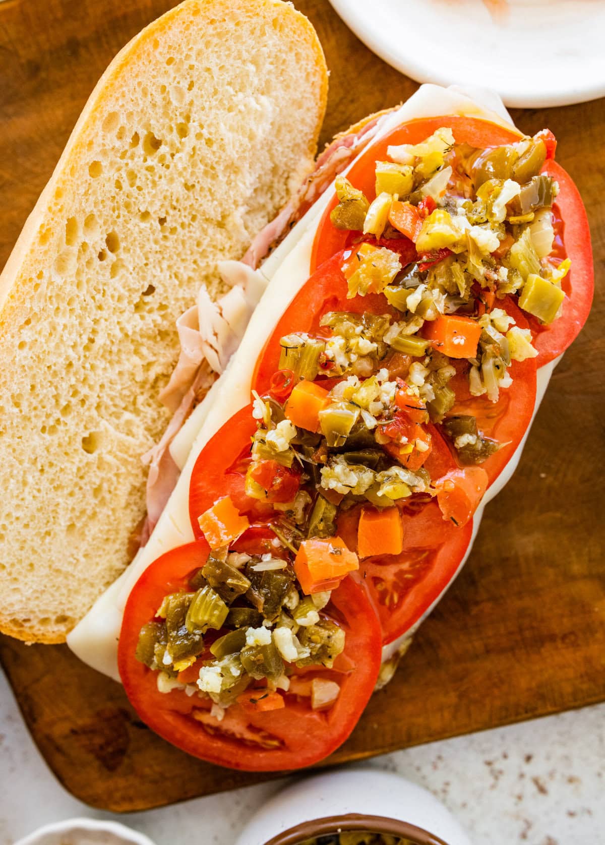 A sandwich with tomatoes and peppers on a wooden cutting board.