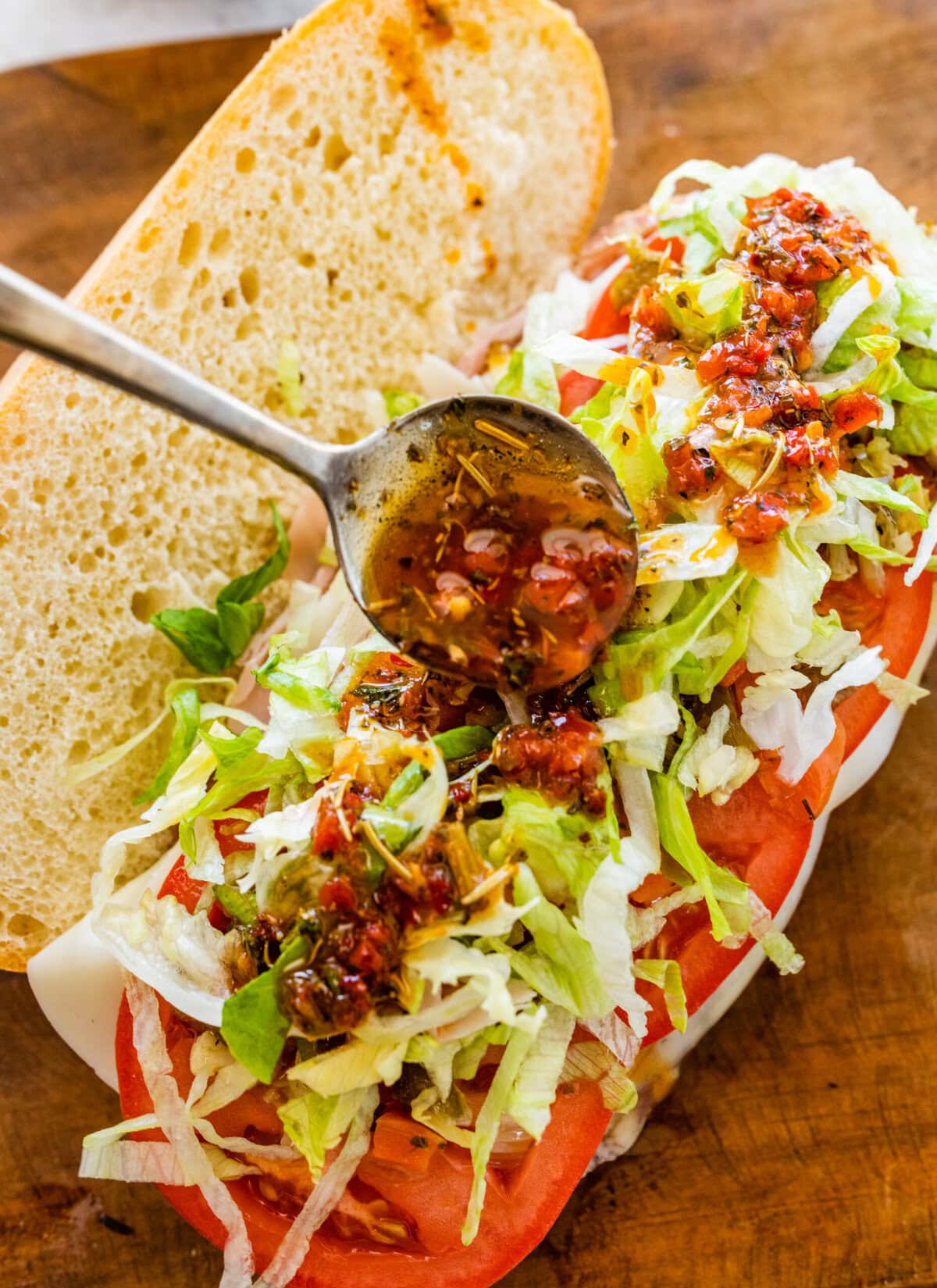 A sandwich with a spoon on top of it pouring dressing on the salad.