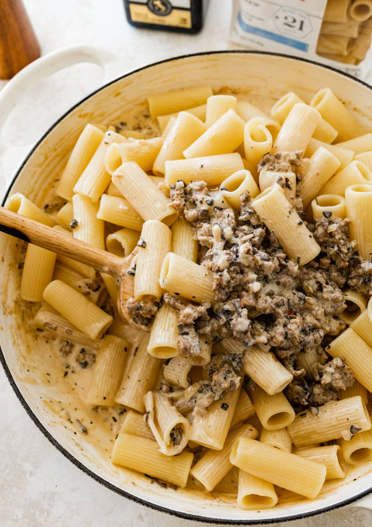 Mixing the cooked pasta with the creamy meat sauce in the pan.