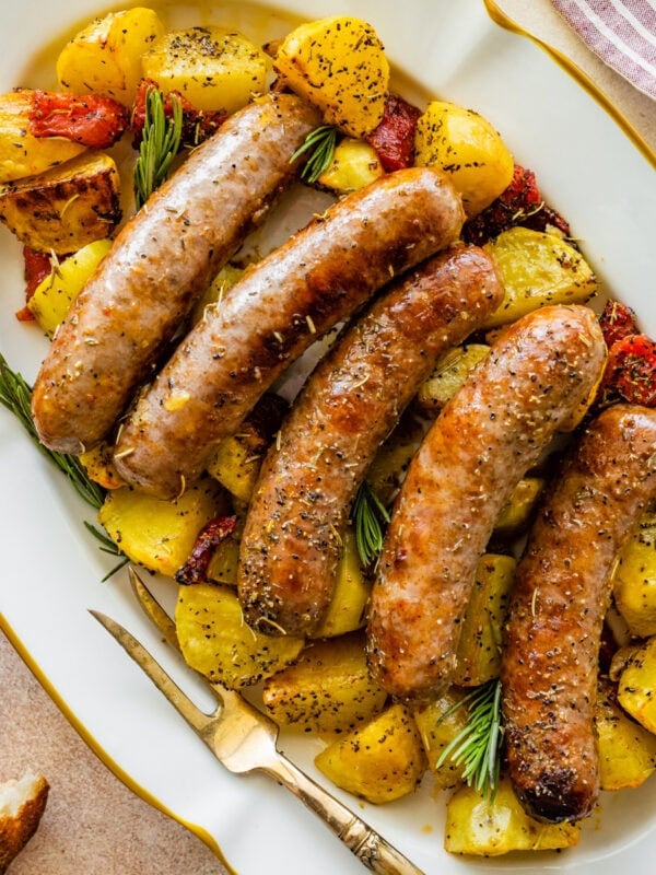 Sausage sheet pan dinner served on a white oval platter with sausages laid on top of the potatoes.