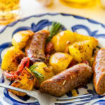 Sausage and potatoes on a white and blue plate with a fork resting to the side.
