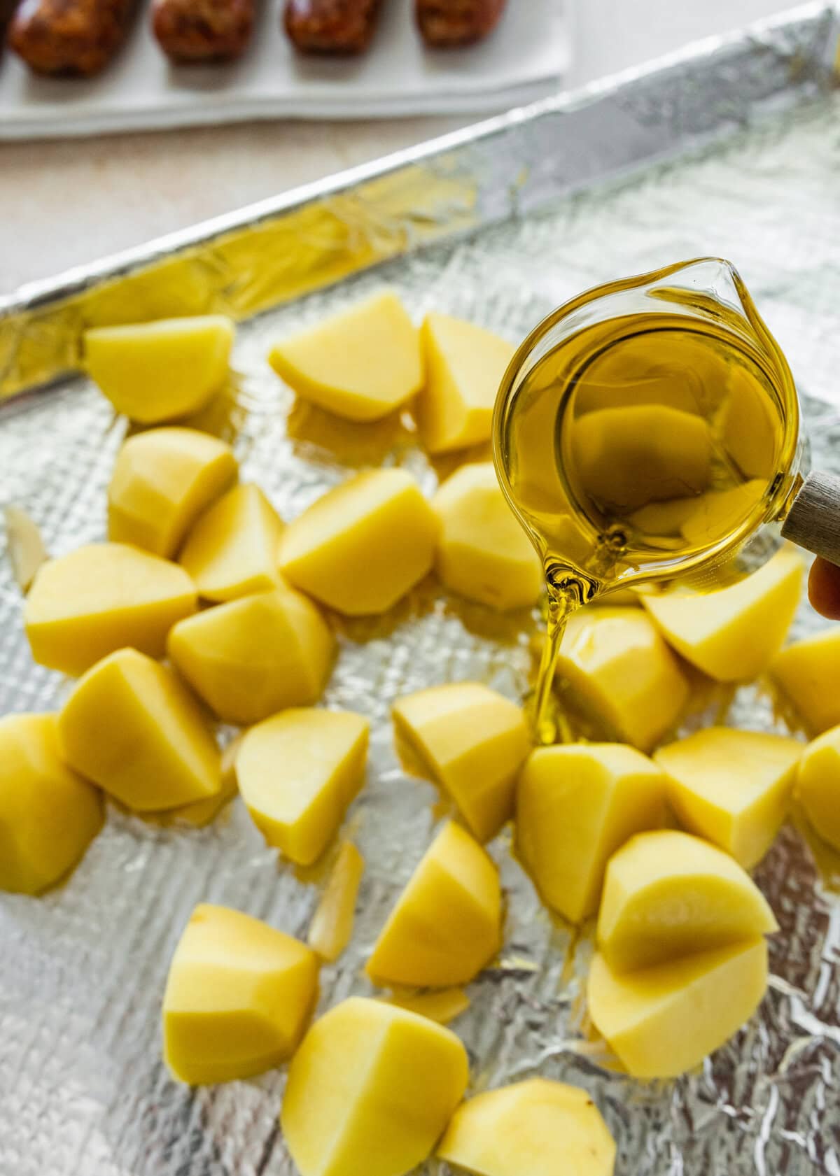 Pouring olive oil over potatoes on a baking sheet.