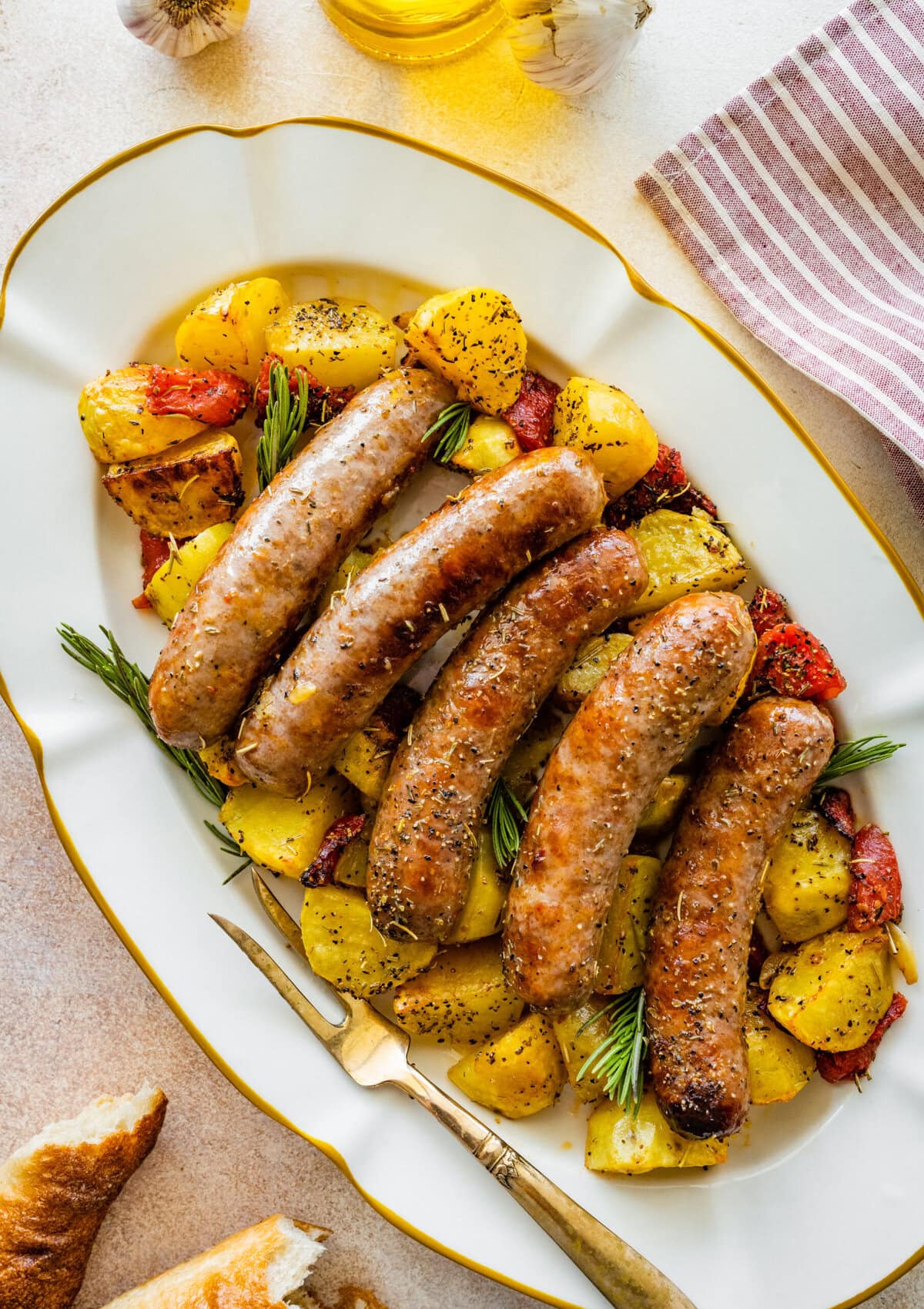 Roasted potatoes and sausages added to a white oval platter.