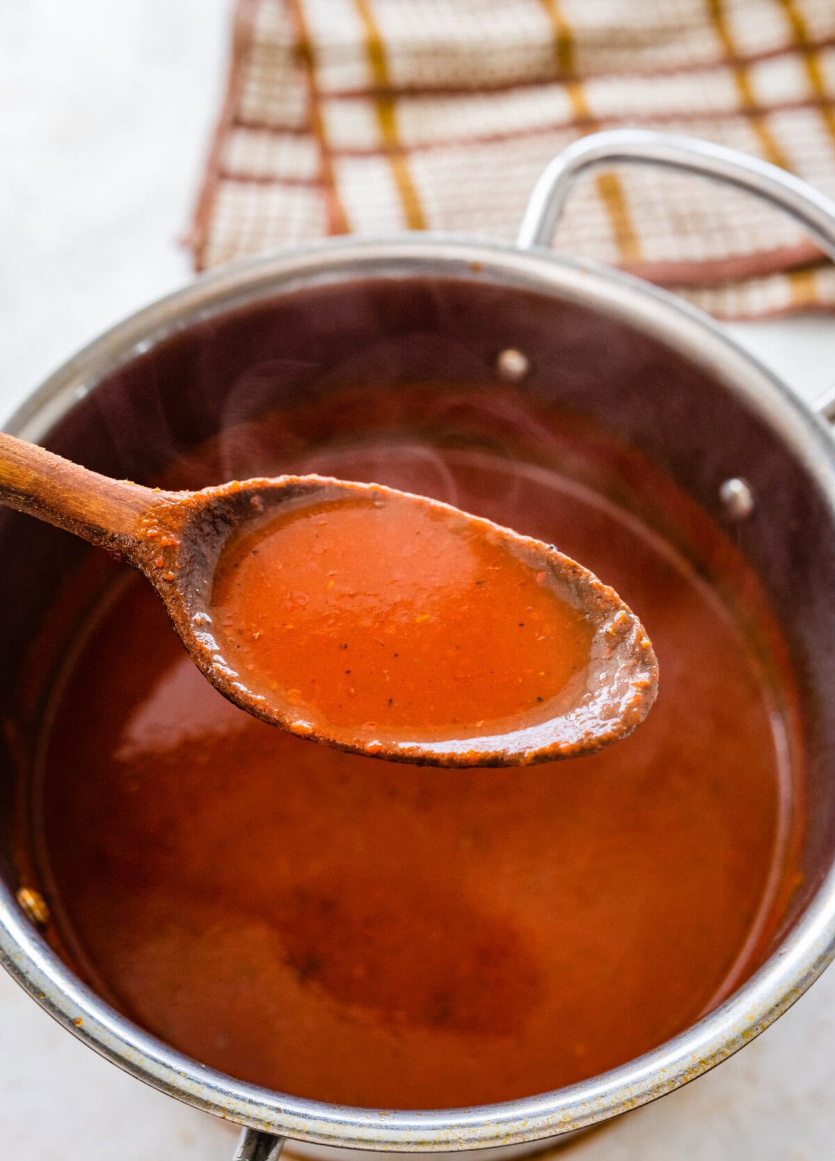 Homemade red enchilada sauce in a pan with a wooden spoon.