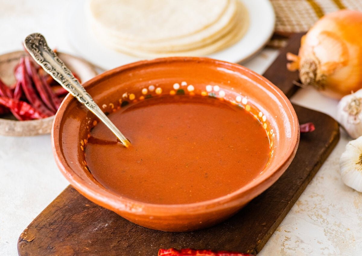 homemade red enchilada sauce in a mexican style bowl with a spoon in it.