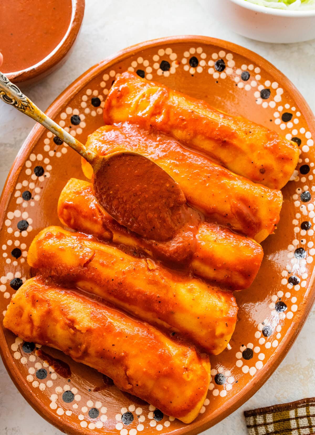 spooning enchilada sauce over chicken enchiladas.