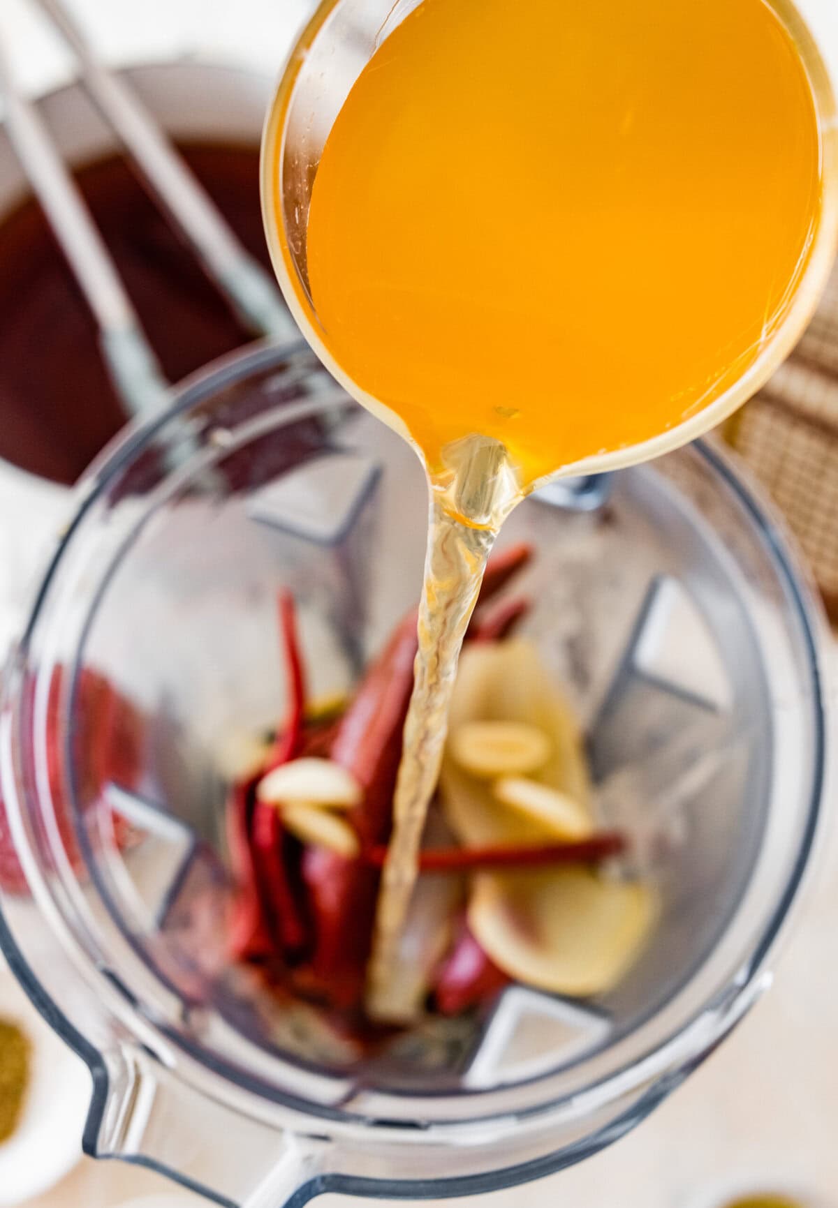 A blender is filled with broth, cooked chilis and spices.