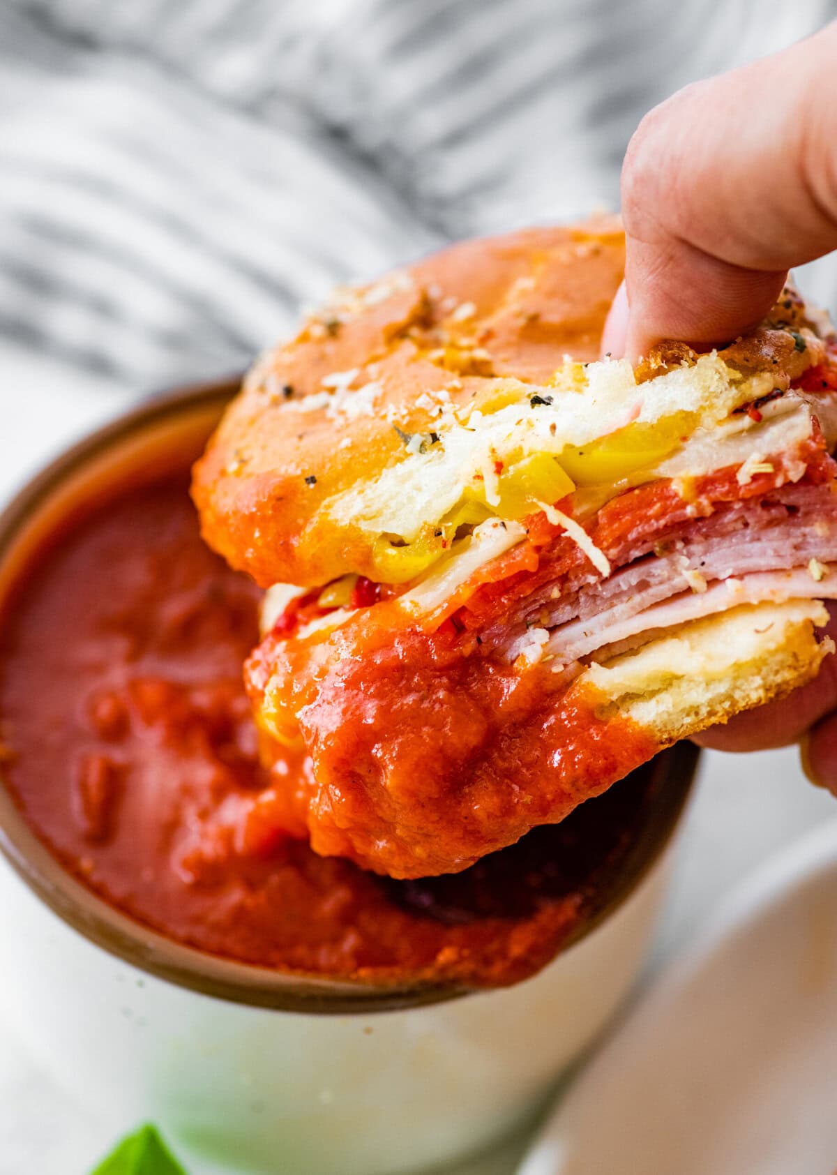 A hand holding a sandwich dipping it in tomato sauce.