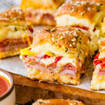 A person holding a sandwich with ham, cheese and peppers.