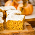 pumpkin bar squares on a cutting board with cream cheese frosting on top.