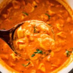 A ladle with tomato tortellini soup holding over the soup pot.