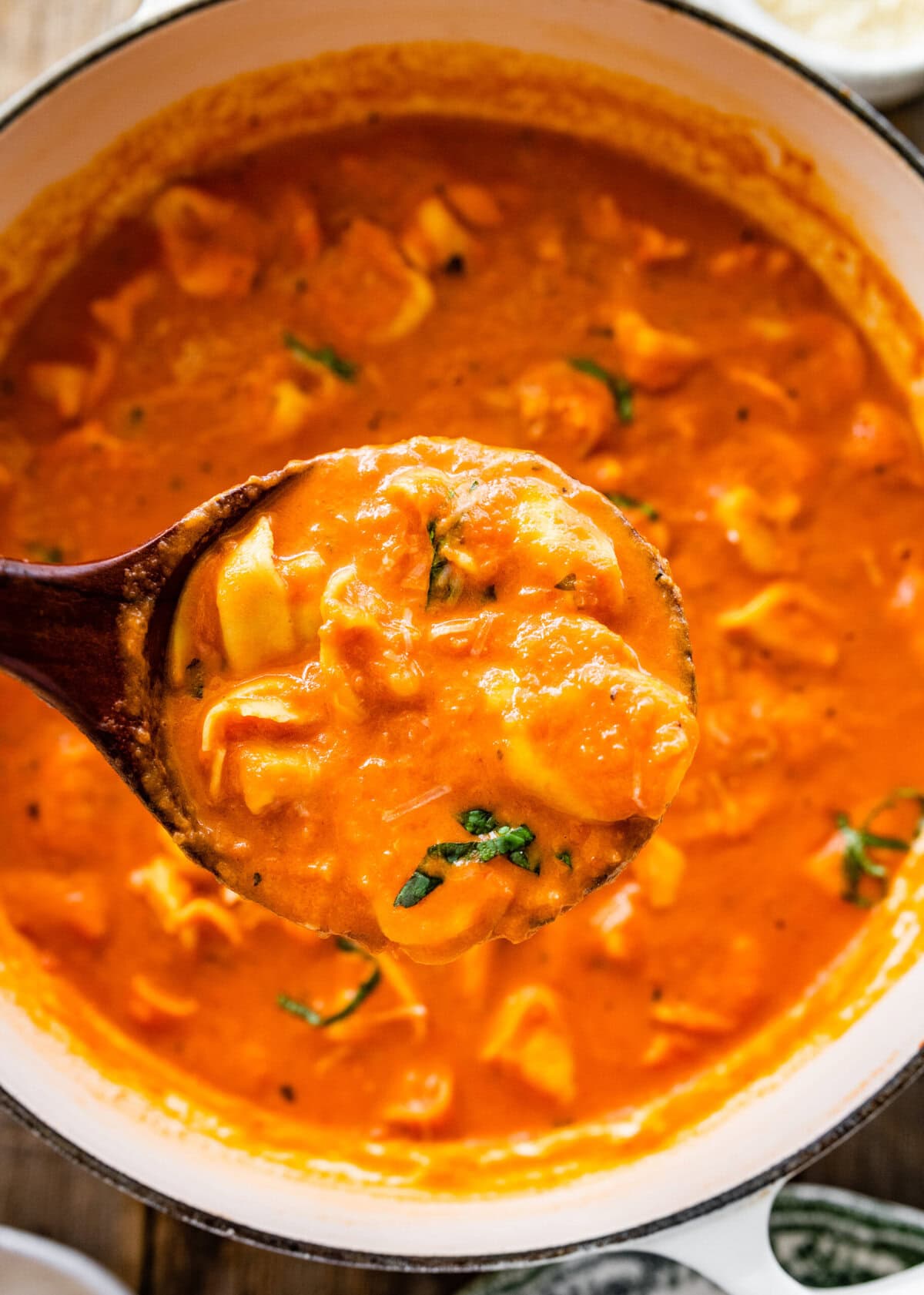 A ladle with tomato tortellini soup holding over the soup pot.