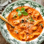 a green and white bowl with tomato tortellini soup recipe. A little fresh basil on top.