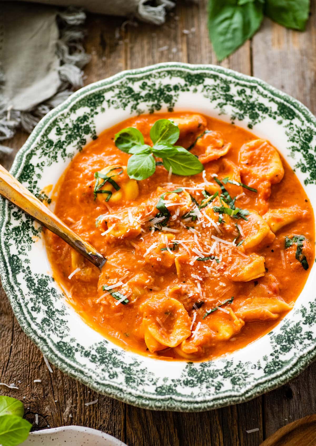 a green and white bowl with tomato tortellini soup recipe. A little fresh basil on top.
