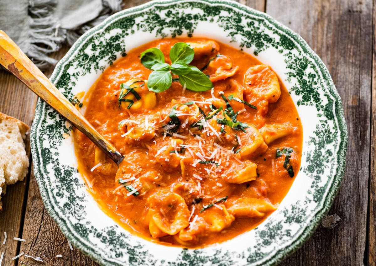 a green and white bowl with tomato tortellini soup recipe. A little fresh basil on top. 
