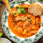 a green and white bowl with tomato tortellini soup recipe. A little fresh basil on top. Crusty bread in the bowl.