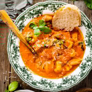 a green and white bowl with tomato tortellini soup recipe. A little fresh basil on top. Crusty bread in the bowl.