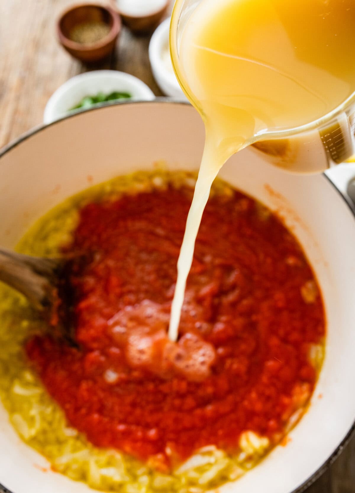 A person pouring broth into a pot of tomato soup.