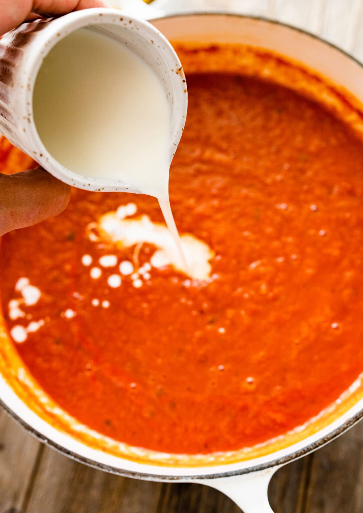 hand pouring a bit of heavy cream into the tomato soup.