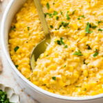 creamed corn recipe in a white bowl with a little parsley on top and extra cheese. Spoon in the bowl.