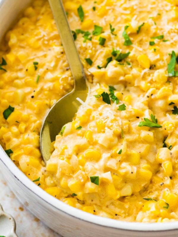 creamed corn recipe in a white bowl with a little parsley on top and extra cheese. Spoon in the bowl.